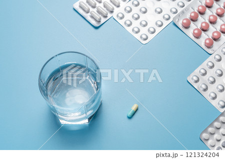 Glass of water and blister packs with capsules and pills. Glass of water and blister packs with capsules and pills. 121324204