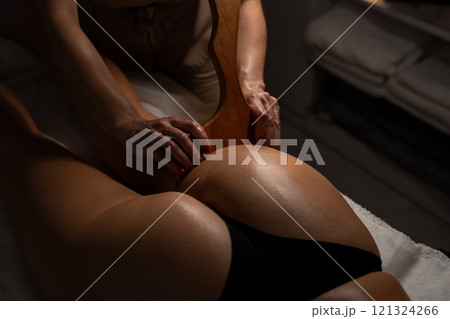 Anti-cellulite massage on the stomach using wooden objects. Massage salon in a dark room. Anti-cellulite massage on the stomach using wooden objects. Massage salon in a dark room. 121324266