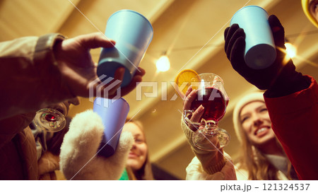 Bottom view of group of people laughing, friends gathering outdoor for holiday celebration, drinking hot drinks, clinking glasses in celebratory toast 121324537