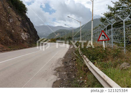 Curved road along the Iran-Azerbaijan border with mountainous backdrop and security fencing 121325384