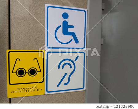 Signs on wall at entrance to building for disabled people, wheelchair sign, icon of deaf person and person with limited vision with braille text, modern accessible area for people with health problem 121325900