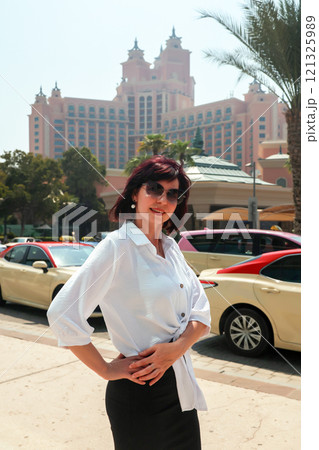 A bright, juicy brunette woman stands near a taxi stand in business clothes 121325989