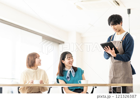 おしゃれなカフェでオーダーを取る男性スタッフと女子2人組 121326387