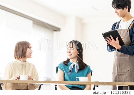 おしゃれなカフェでオーダーを取る男性スタッフと女子2人組 121326388