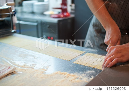 A chef prepares pasta by cutting and rolling the raw dough on a metal countertop. 121326908