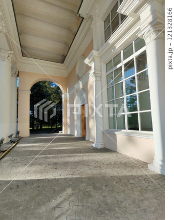 A neoclassical colonnade with tall white pillars, large windows, and textured flooring under a vaulted ceiling. The play of natural light enhances the grandeur of the design. 121328166