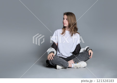 A girl in a casual outfit sits cross-legged, lost in thought. This image highlights the blend of innocence and emerging maturity, symbolizing the journey of self-discovery and individuality. 121328183