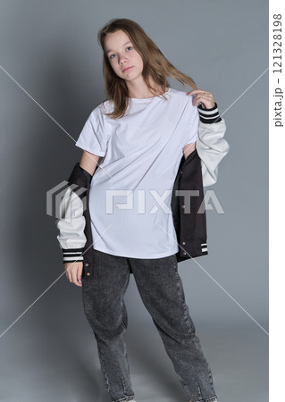 A girl stands in a relaxed pose with her jacket over her shoulders, gazing down. This image embodies the calm confidence of adolescence and the journey toward self-discovery. 121328198