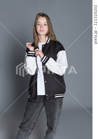 A teenage girl in profile with a varsity jacket resting on her shoulder, giving off a relaxed vibe. Her natural expression highlights youthful energy and individuality. 121328202