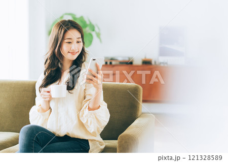 ソファに座ってコーヒーを飲みながらスマホを見る女性 ソファに座ってコーヒーを飲みながらスマホを見る女性 121328589