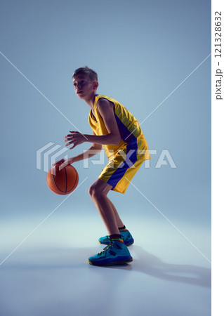 Boy, dressed bright yellow blue uniform training dribbling technique against grey studio background. Competitive spirit. Boy, dressed bright yellow blue uniform training dribbling technique against grey studio background. Competitive spirit. 121328632