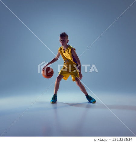 Little boy dressed sport uniform training basketball techniques against grey studio background. Little champion. 121328634