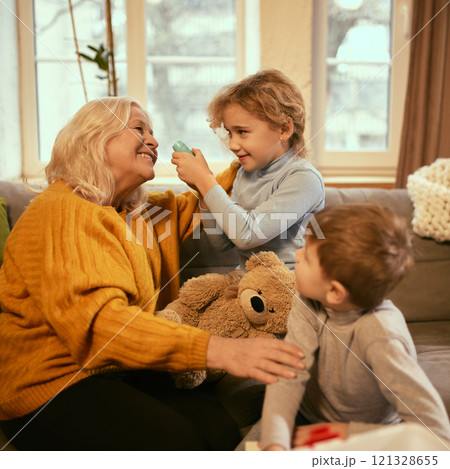 Boy playfully examines grandmother's heartbeat while girl holds teddy bear, combining learning with imaginative play to understand health concepts. 121328655