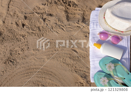 Beach essentials: towel, hat, sunglasses, sunscreen, and sandals on sandy beach Beach essentials: towel, hat, sunglasses, sunscreen, and sandals on sandy beach 121329808