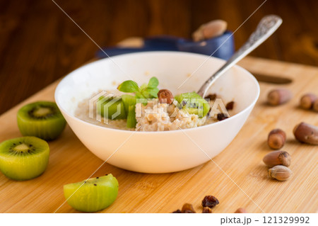 cooked oatmeal with kiwi, honey and nuts in a bowl on a wooden table 121329992