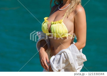 Blonde woman with big breasts in a yellow swimsuit on the beach. Portrait of a young woman with a beautiful body. Sexy model showing bra Blonde woman with big breasts in a yellow swimsuit on the beach. Portrait of a young woman with a beautiful body. Sexy model showing bra 121330344