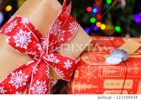 Beautifully wrapped gifts adorned with red ribbons are placed near sparkling Christmas tree with colorful lights during New Year 121330434