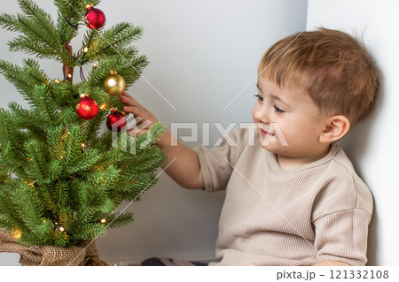 A small child looks at the New Year's decorations on a green New Year's tree A small child looks at the New Year's decorations on a green New Year's tree 121332108