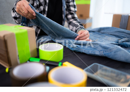 Young Woman Folds Jeans Jacket, Reflecting The Concept Of Clothing Order Young Woman Folds Jeans Jacket, Reflecting The Concept Of Clothing Order 121332472