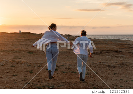 Couple Sunset Beach Run - Two people run towards the ocean during a sunset on a beach. Couple Sunset Beach Run - Two people run towards the ocean during a sunset on a beach. 121332582