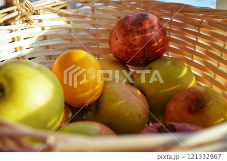 Close up photo sun rays on a wicker basket with apples pomegranates and oranges view from inside the basket. High quality photo Close up photo sun rays on a wicker basket with apples pomegranates and oranges view from inside the basket. High quality photo 121332967