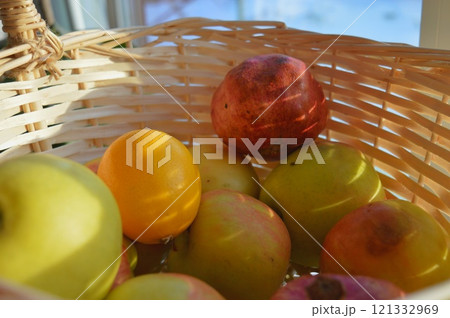 Close up photo sun rays on a wicker basket with apples pomegranates and oranges view from inside the basket. High quality photo Close up photo sun rays on a wicker basket with apples pomegranates and oranges view from inside the basket. High quality photo 121332969