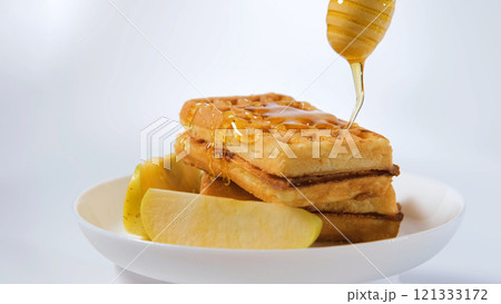 Hand pouring honey on fluffy waffles with fresh apples, breakfast concept Hand pouring honey on fluffy waffles with fresh apples, breakfast concept 121333172