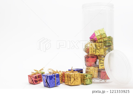 Colorful miniature gift boxes lie in a clear plastic jar and on its side against a white background. Colorful miniature gift boxes lie in a clear plastic jar and on its side against a white background. 121333925