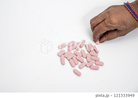 Female hand taking a pink pill on a white background, top view Female hand taking a pink pill on a white background, top view 121333949