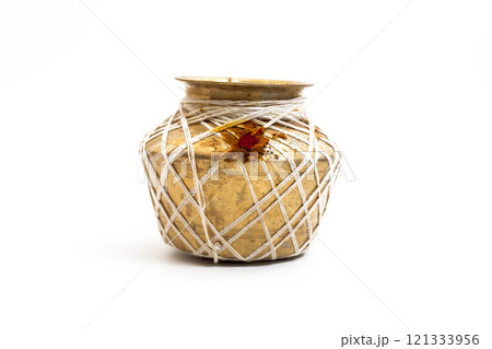Golden brass pot decorated with string and red ritual powder on a white background 121333956