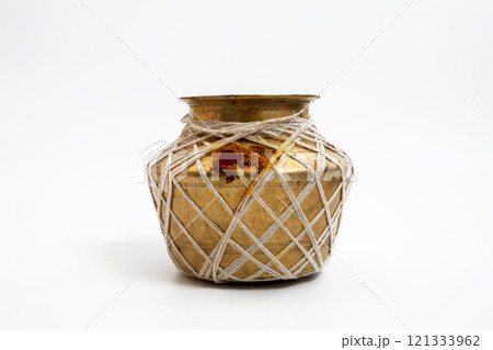 Golden brass pot decorated with string and red ritual powder on a white background 121333962
