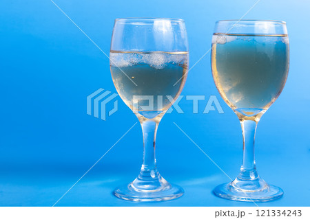 Close-Up of Two Glasses of White Wine with Ice on a Vibrant Blue Background, Copy Space for Your Text Close-Up of Two Glasses of White Wine with Ice on a Vibrant Blue Background, Copy Space for Your Text 121334243