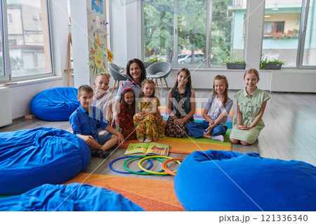 A happy female teacher sitting and playing hand games with a group of little schoolchildren 121336340