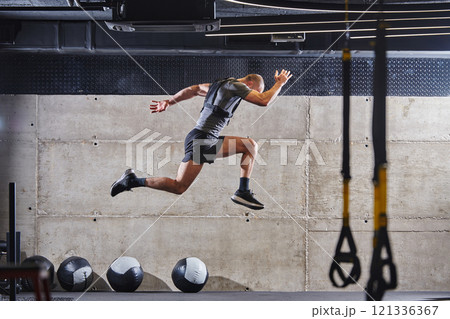 A muscular man captured in air as he jumps in a modern gym, showcasing his athleticism, power, and determination through a highintensity fitness routine A muscular man captured in air as he jumps in a modern gym, showcasing his athleticism, power, and determination through a highintensity fitness routine 121336367