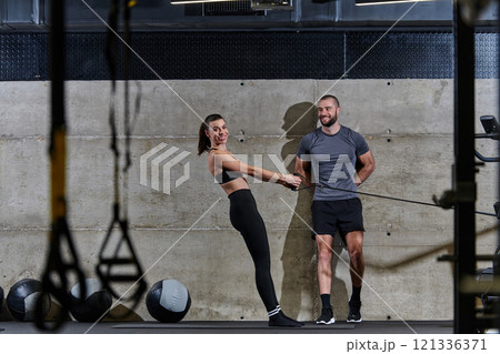 A muscular man assisting a fit woman in a modern gym as they engage in various body exercises and muscle stretches, showcasing their dedication to fitness and benefiting from teamwork and support A muscular man assisting a fit woman in a modern gym as they engage in various body exercises and muscle stretches, showcasing their dedication to fitness and benefiting from teamwork and support 121336371