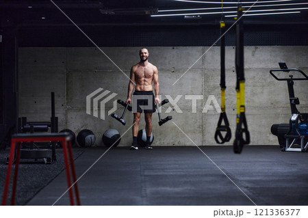 A muscular man performs shoulder exercises in a modern gym, showcasing his strength and dedication to fitness. 121336377