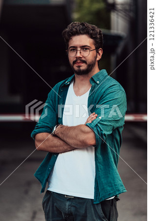 A successful young businessman in a shirt, with crossed arms, poses outdoors, confident expression on his face. 121336421