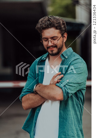 A successful young businessman in a shirt, with crossed arms, poses outdoors, confident expression on his face. A successful young businessman in a shirt, with crossed arms, poses outdoors, confident expression on his face. 121336434