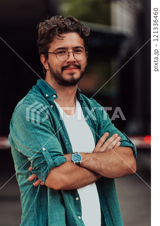 A successful young businessman in a shirt, with crossed arms, poses outdoors, confident expression on his face. 121336460
