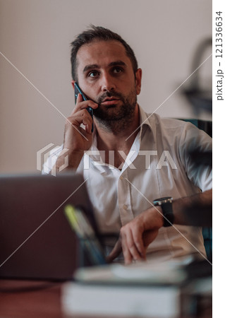 A businessman talking on his smartphone while seated in an office, showcasing his professional demeanor and active communication. 121336634