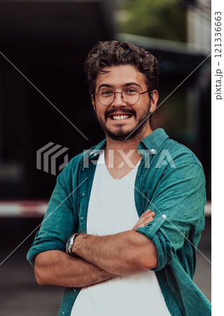 A successful young businessman in a shirt, with crossed arms, poses outdoors, confident expression on his face. A successful young businessman in a shirt, with crossed arms, poses outdoors, confident expression on his face. 121336663