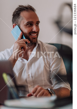A businessman talking on his smartphone while seated in an office, showcasing his professional demeanor and active communication. 121336684