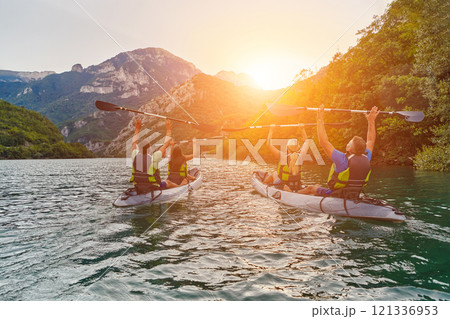 A group of friends enjoying fun and kayaking exploring the calm river, surrounding forest and large natural river canyons during an idyllic sunset. A group of friends enjoying fun and kayaking exploring the calm river, surrounding forest and large natural river canyons during an idyllic sunset. 121336953