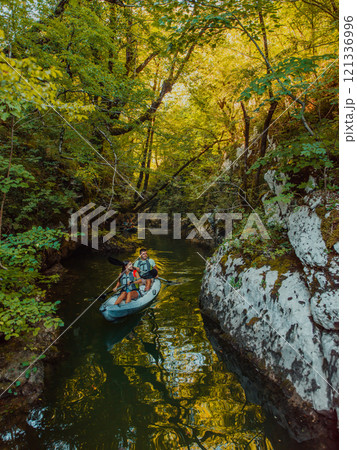 A young couple enjoying an idyllic kayak ride in the middle of a beautiful river surrounded by forest greenery A young couple enjoying an idyllic kayak ride in the middle of a beautiful river surrounded by forest greenery 121336996