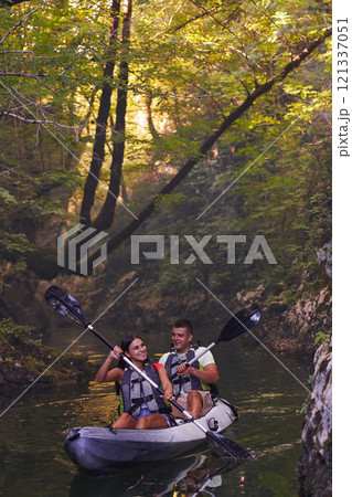 A young couple enjoying an idyllic kayak ride in the middle of a beautiful river surrounded by forest greenery 121337051