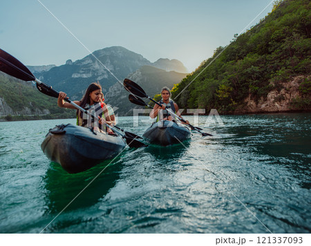 A group of friends enjoying fun and kayaking exploring the calm river, surrounding forest and large natural river canyons during an idyllic sunset. 121337093