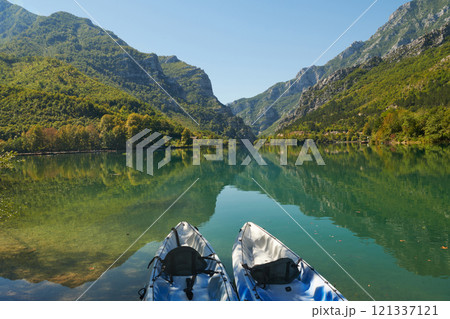 An idyllic photo of two kayaks on the river bank. In the background of green forest area and mountains 121337121