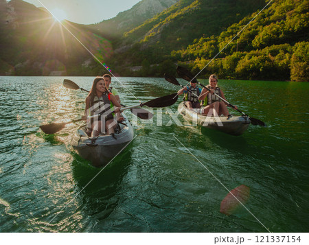 A group of friends enjoying fun and kayaking exploring the calm river, surrounding forest and large natural river canyons during an idyllic sunset. 121337154