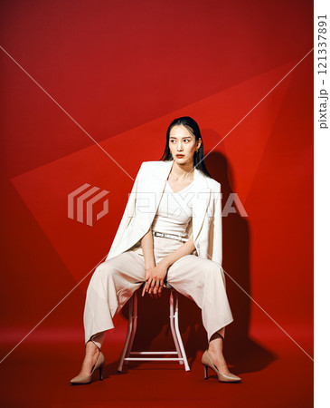 真っ赤な背景紙をバックに白いパンツスーツを着たキャリアウーマン 真っ赤な背景紙をバックに白いパンツスーツを着たキャリアウーマン 121337891