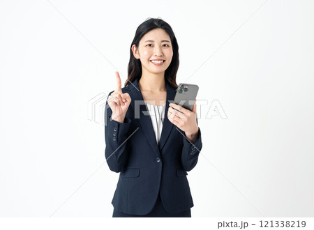 スマホを持って人差し指でポイントのサインを出すスーツ姿の若い女性 121338219